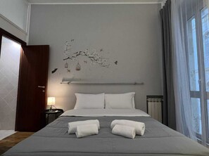 A hotel room with a large bed, two pillows, a nightstand with a lamp, and a wall decoration. - Room Aurea Guest House (Rome)