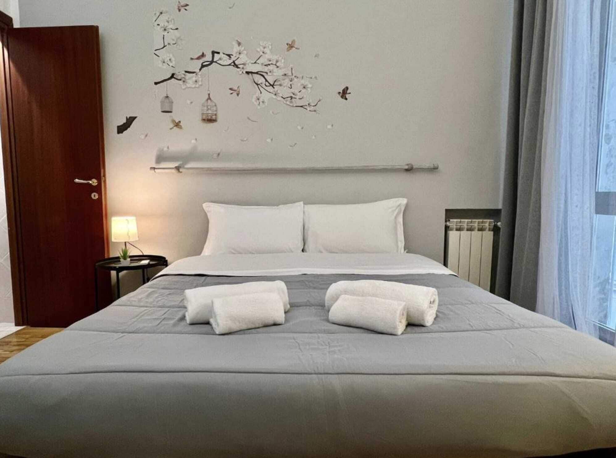 A hotel room with a bed, two pillows, a nightstand with a lamp, and a wall decoration of birds and flowers.