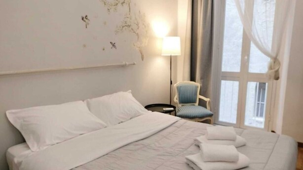 A hotel room with a large bed, a chair, a bedside table, and a lamp.