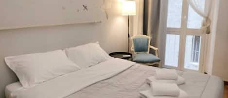 Una habitación de hotel con una cama grande, una silla, una mesita de noche y una lámpara.