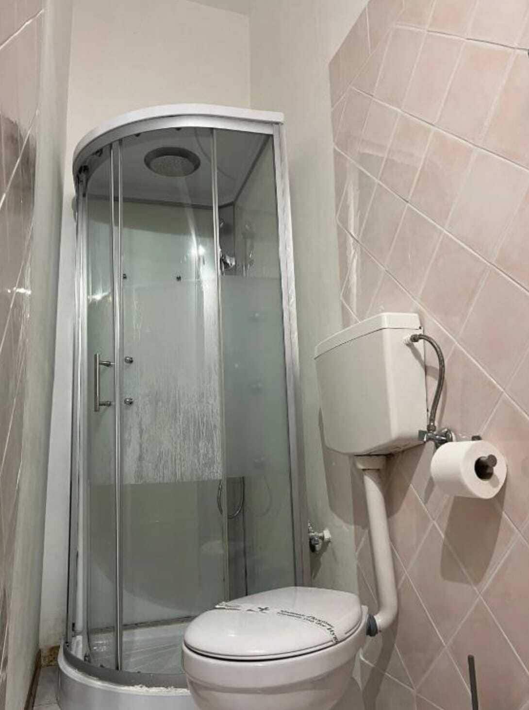 Une salle de bain avec une douche à parois de verre, des toilettes et un porte-rouleau de papier toilette fixé au mur.