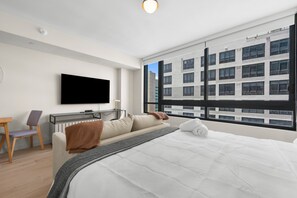 Ein modernes Hotelzimmer mit einem großen Bett, einem Schreibtisch mit Stuhl, einem flachbildfernseher an der Wand und einem großen Fenster mit Blick auf die Stadt.