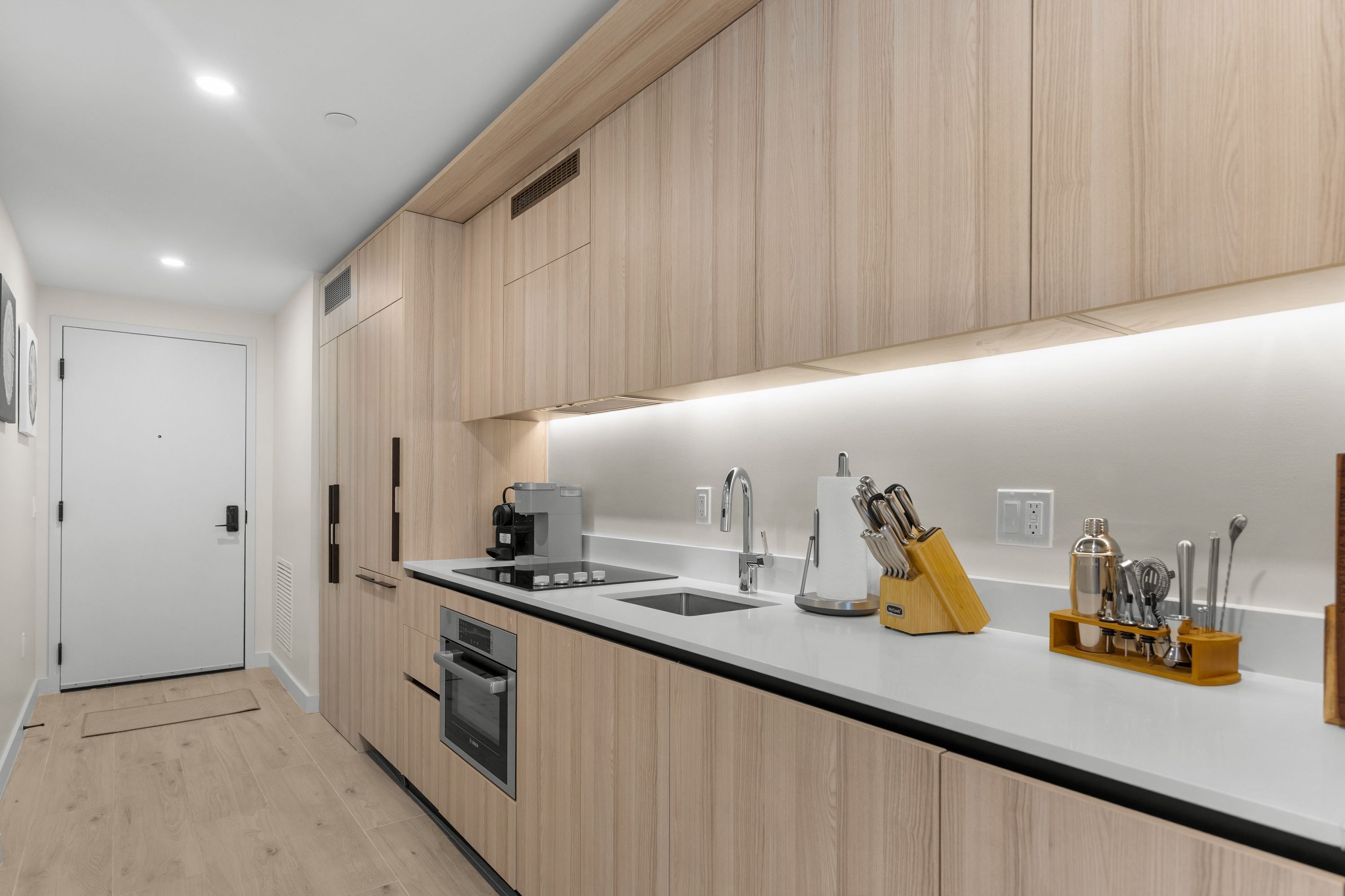 A modern kitchen with wooden cabinets, a black countertop, a coffee machine, a sink, and a knife block.