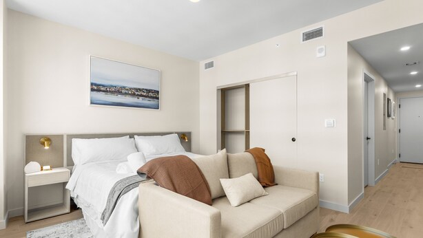 Ein modernes Schlafzimmer mit Bett, Nachttischen, einer Couch und Blick auf eine Stadtlandschaft.