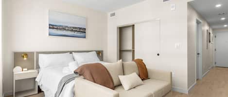 A modern bedroom with a bed, bedside tables, a sofa, and a view of a cityscape.