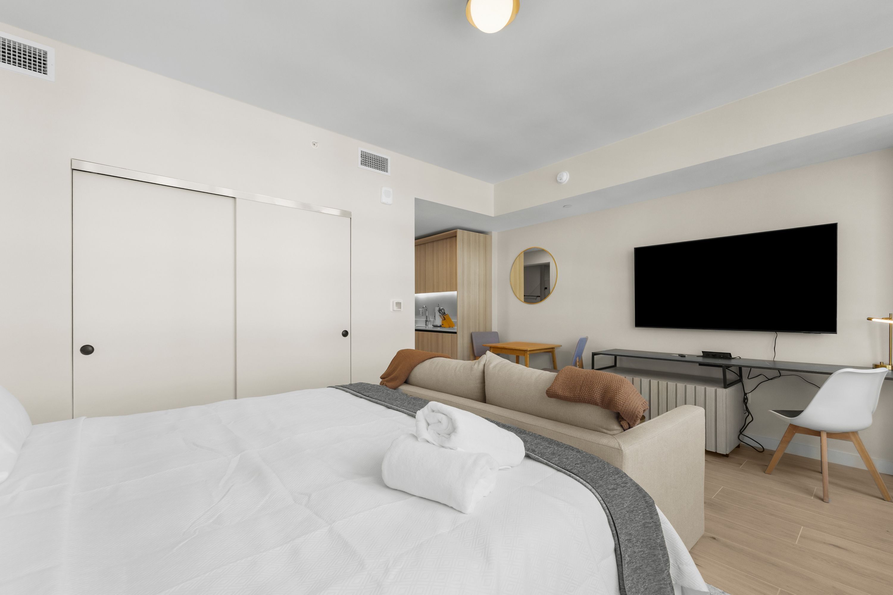 A modern hotel room with a large bed, a desk, a television, and a bathroom visible in the background.