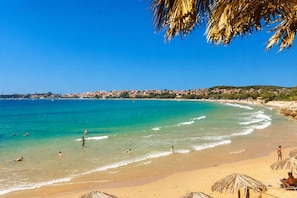 A beach with clear turquoise water, a sandy shore, and a distant town with buildings. - Stone House Central Filiatra - 7min From the Beach (Trifylia)