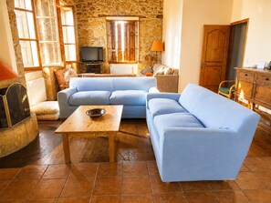 A living room with a blue sofa, a wooden coffee table, and a stone wall. - Stone House Central Filiatra - 7min From the Beach (Trifylia)