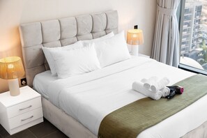 A neatly made bed with white linens, two bedside lamps, and a view of the city through a window. - Stayshort - Meydan One Sleeps 4 Close to Meydan Racecourse (Dubai)