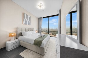A modern bedroom with a large bed, a nightstand, a lamp, a painting, and a city view. - Stayshort - Meydan One Sleeps 4 Close to Meydan Racecourse (Dubai)