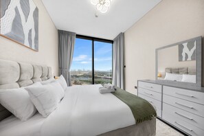 A modern bedroom with a large bed, a dresser, and a city view. - Stayshort - Meydan One Sleeps 4 Close to Meydan Racecourse (Dubai)