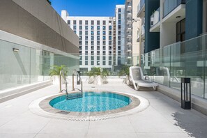 A rooftop pool area with a clear blue pool, lounge chairs, and a modern building in the background. - Stayshort - Meydan One Sleeps 4 Close to Meydan Racecourse (Dubai)