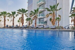 A swimming pool with lounge chairs and palm trees. - Stayshort - Cozy Studio in Damac Hills That Sleeps 2 (Dubai)