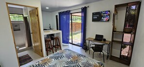 A room with a bed, a desk with a laptop, a TV, and a dining area with stools. - Casita Ola Negra, just minutes from the beach—a cozy private studio for 2 people (Puerto Viejo de Talamanca)