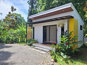 A modern house with a covered porch, surrounded by lush greenery and a gravel driveway. - Casita Ola Negra, just minutes from the beach—a cozy private studio for 2 people (Puerto Viejo de Talamanca)