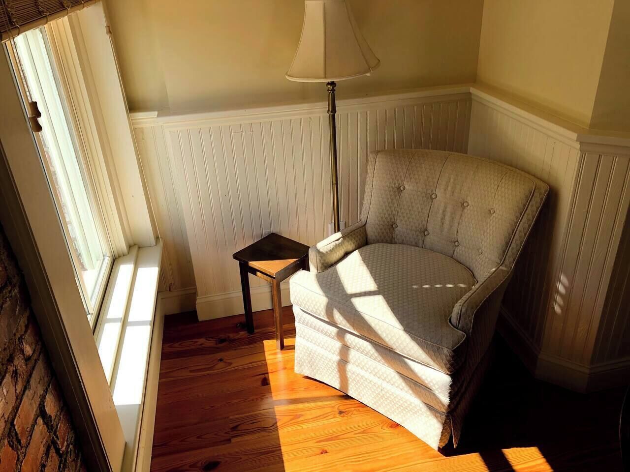 Une pièce avec un plancher en bois, une chaise, une petite table et une lampe.