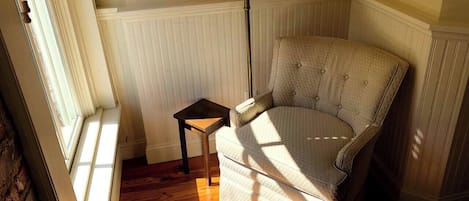 Una habitación con piso de madera, una silla, una mesita y una lámpara.