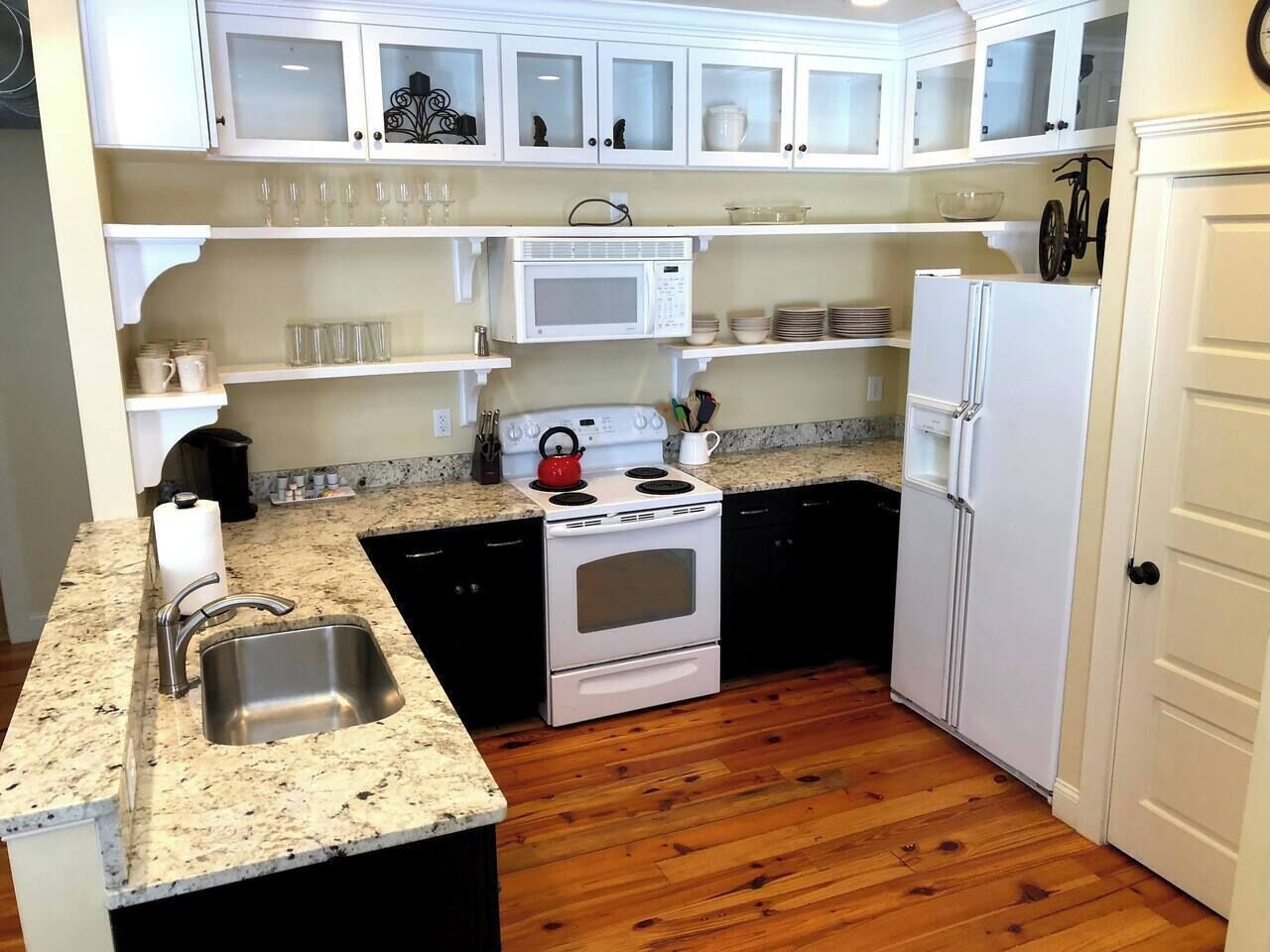 A compact kitchen with white cabinets, a stainless steel sink, a microwave, a stove, and a refrigerator.