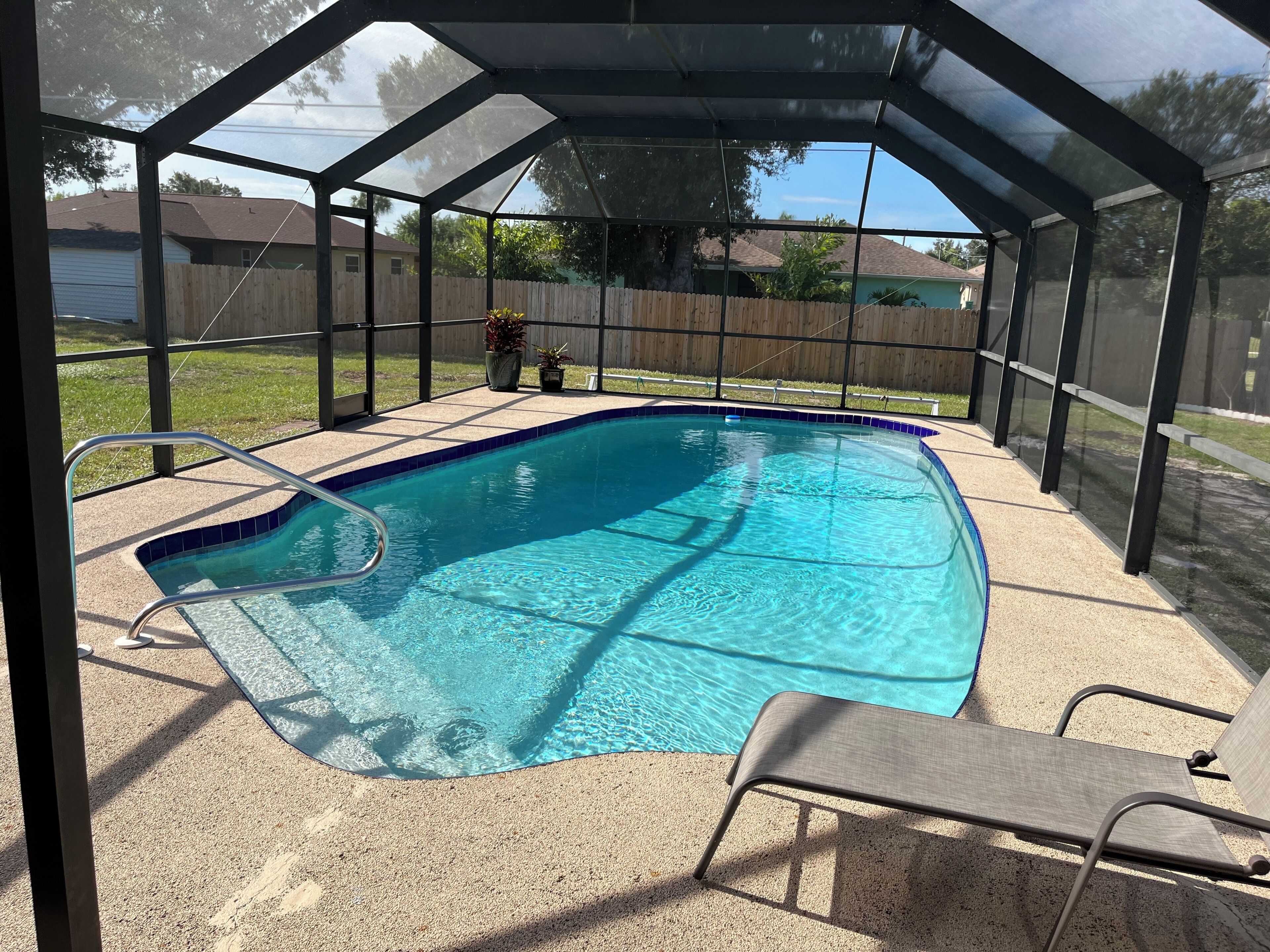 A covered swimming pool with a metal railing and a lounge chair.