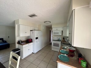 A compact kitchen with a refrigerator, microwave, stove, and a small dining area with a chair and a trash bin. - Winds And Waves 
Delightful 2-bedroom house in Englewood for your getaway (Englewood)