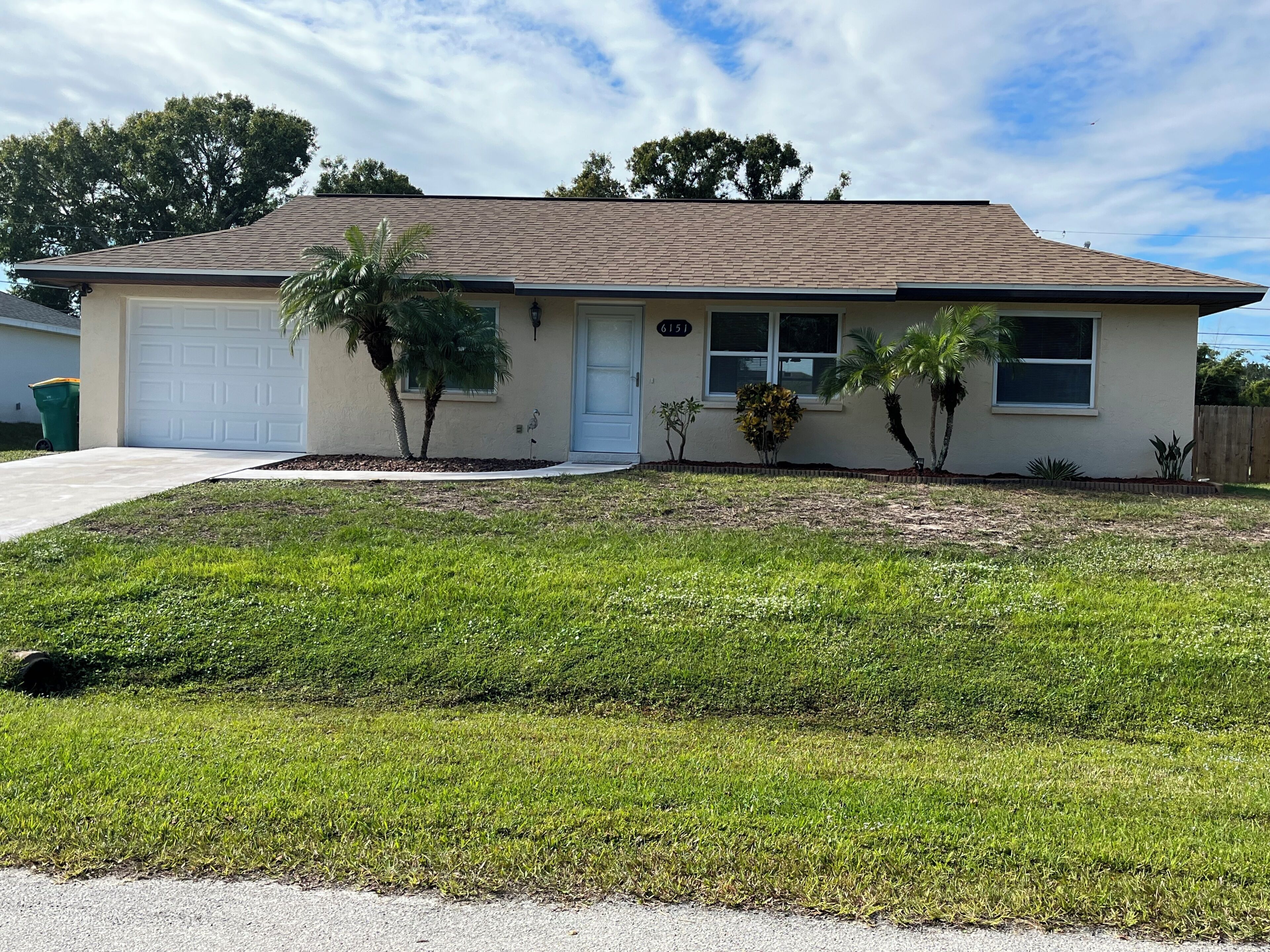 A single-story house with a garage, a well-maintained lawn, and a small garden with palm trees.