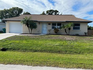 A single-story house with a garage, a well-maintained lawn, and a small garden with palm trees. - Winds And Waves 
Delightful 2-bedroom house in Englewood for your getaway (Englewood)