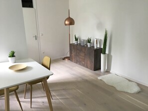 Ein Essbereich mit weißem Tisch, einem goldfarbenen Stuhl, Holzboden, einem Schrank mit Topfpflanzen und einer Pendelleuchte.