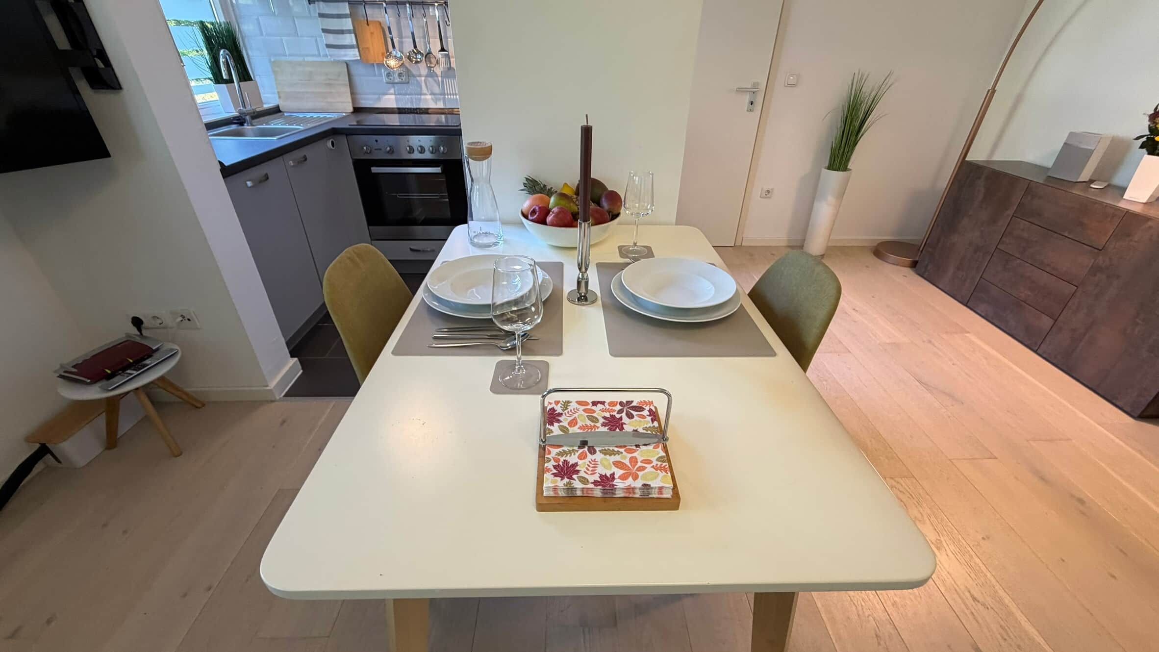 A dining table set with plates, glasses, and cutlery, a vase with flowers, and a decorative box.