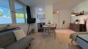 A modern living room with a sofa, a dining table with chairs, a kitchen area, and a bed. - Stylish apartment in Munich right next to Südpark (München)