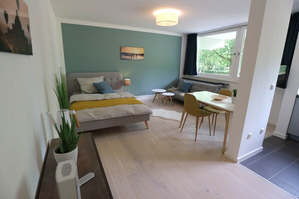 A modern bedroom with a bed, bedside table, and a window with a view of greenery. - Stylish apartment in Munich right next to Südpark (München)