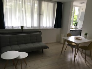 A living room with a grey sofa, two round tables, a dining table with chairs, and a kitchen visible through an open door. - Stylish apartment in Munich right next to Südpark (München)
