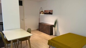A room with a wooden desk, a white table, a bed with a mustard-colored blanket, a lamp, and a painting on the wall. - Stylish apartment in Munich right next to Südpark (München)