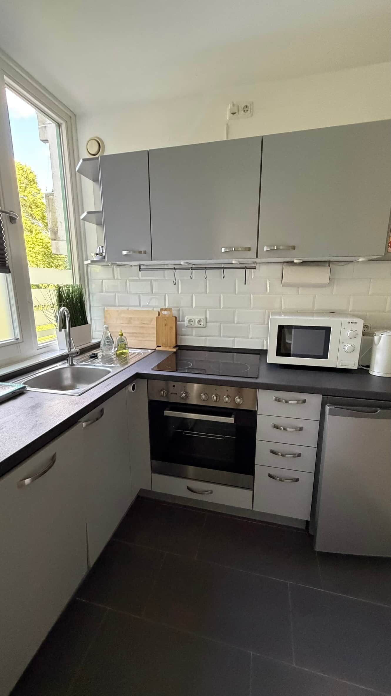 A modern kitchen with grey cabinets, a built-in oven, a microwave, and a sink.