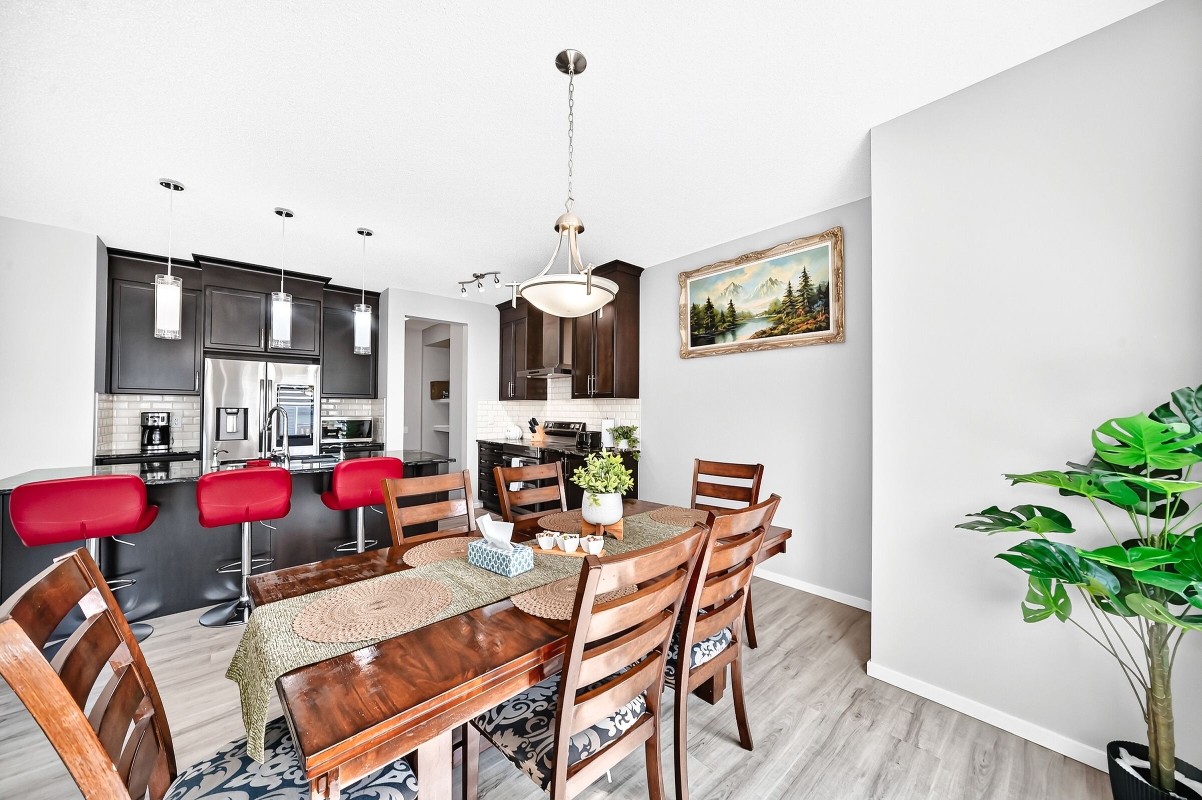 A modern kitchen with dark cabinets, stainless steel appliances, and a dining area with a wooden table and red bar stools.