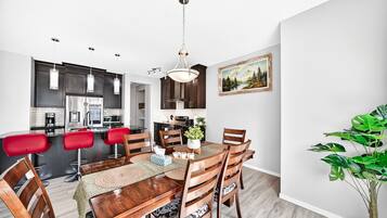 A modern kitchen with dark cabinets, stainless steel appliances, and a dining area with a wooden table and red bar stools.