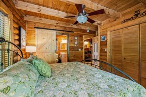 A wooden cabin interior with a bed, a ceiling fan, and a bathroom visible through an open door. - Cabin w/ Hot Tub · Hear the Dollywood Whistle (Sevierville)