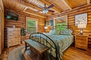 A wooden cabin bedroom with a bed, a bench, a dresser, a television, and a ceiling fan. - Cabin w/ Hot Tub · Hear the Dollywood Whistle (Sevierville)