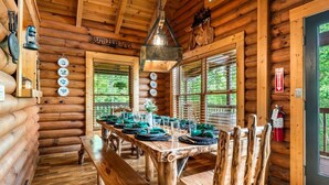 Ein Holzblockhaus-Interieur mit Esstisch für vier Personen, einer Bank und einem Kamin.