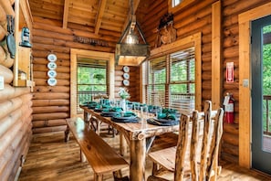 Ein Holzblockhaus-Interieur mit Esstisch für vier Personen, einer Bank und einem Kamin.