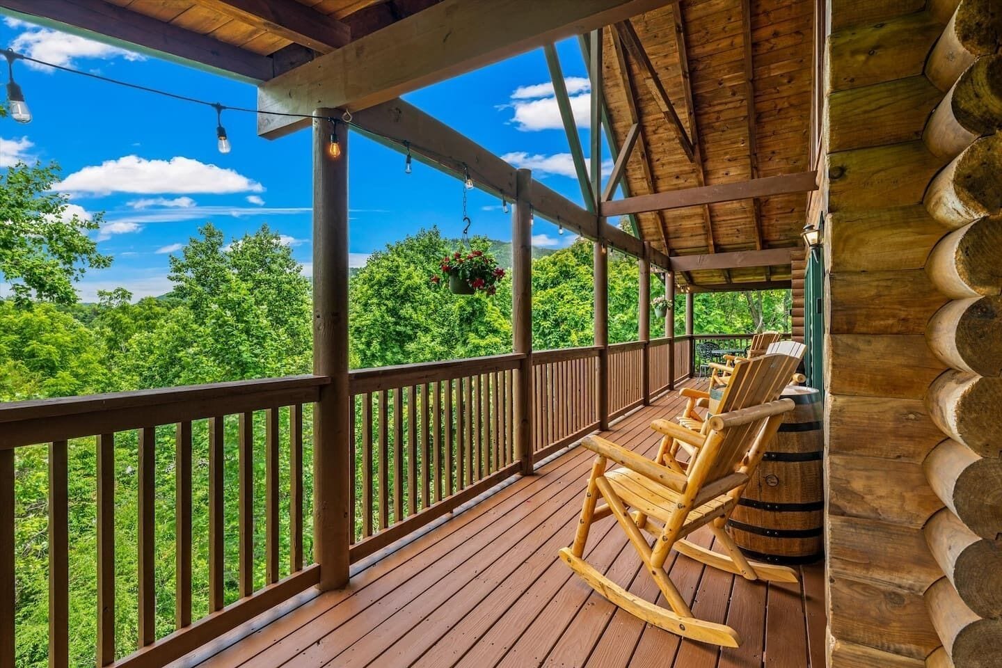 A wooden deck with a railing, rocking chairs, and hanging flower baskets.