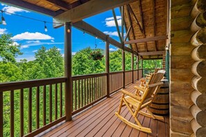 Une terrasse en bois avec une balustrade, des fauteuils à bascule et des jardinières suspendues.