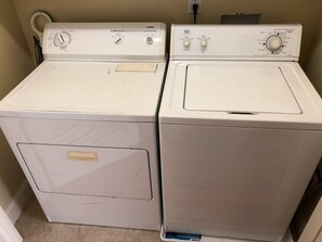 Two stacked white front-loading washing machines in a room with a beige wall and a power outlet above them. - Downtown Wake Forest Loft #2 (Wake Forest)