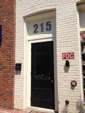 A building with a white brick facade, a black door, and a sign indicating the address as 215. - Downtown Wake Forest Loft #2 (Wake Forest)