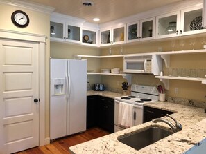 Una cocina con armarios blancos, un refrigerador, un microondas, una estufa y un lavaplatos.