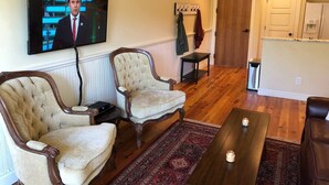 Un salon avec deux fauteuils, une table basse et un téléviseur fixé au mur.