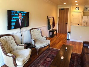 Una sala de estar con dos sillones, una mesa de centro y un televisor montado en la pared.