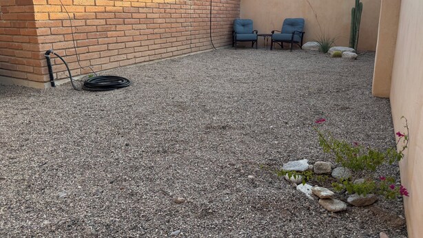 Un patio de grava con dos sillas, un cactus y una manguera.