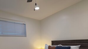 Un dormitorio con cama, mesita de noche, lámpara y ventana con persianas.