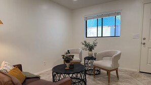 Una sala de estar con un sofá de cuero marrón, dos sillones blancos, una mesa de centro redonda negra y una planta en maceta.