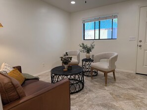 Ein Wohnzimmer mit einem braunen Ledersofa, zwei weißen Sesseln, einem runden schwarzen Couchtisch und einer Topfpflanze.